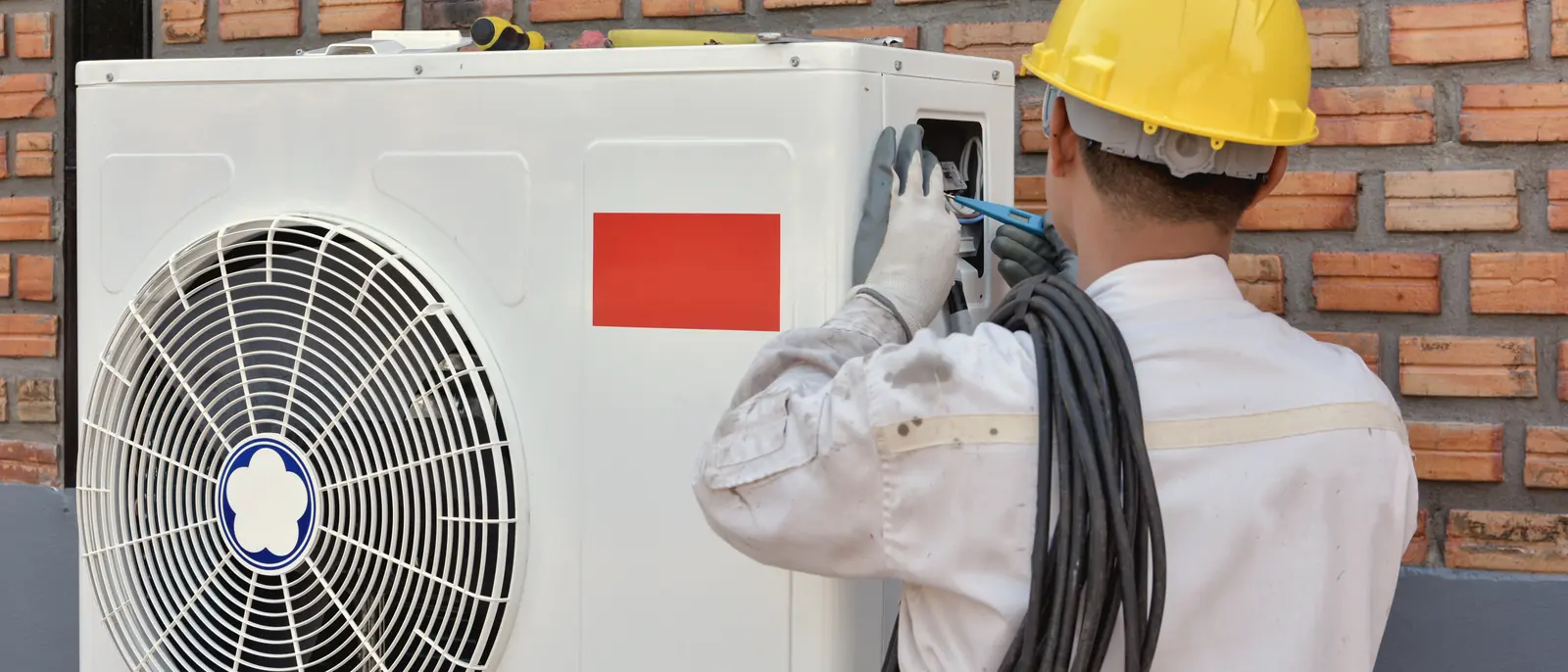 Technicien installant l'unité extérieure d'une thermopompe sur un mur de brique