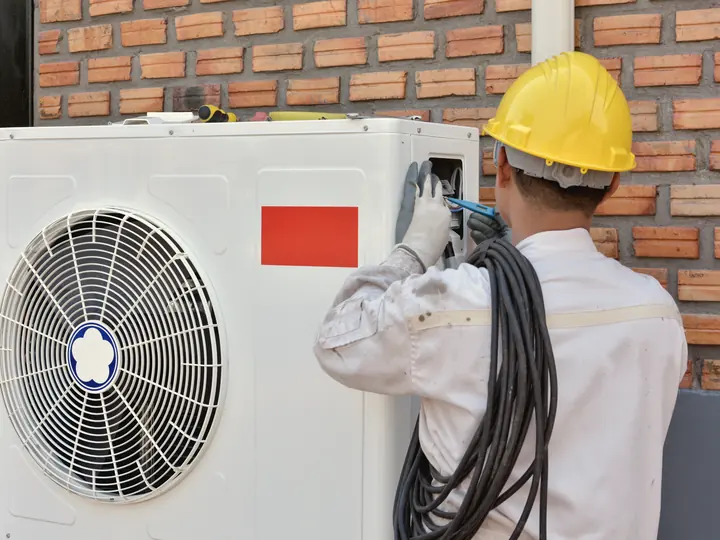 Technicien installant l'unité extérieure d'une thermopompe sur un mur de brique