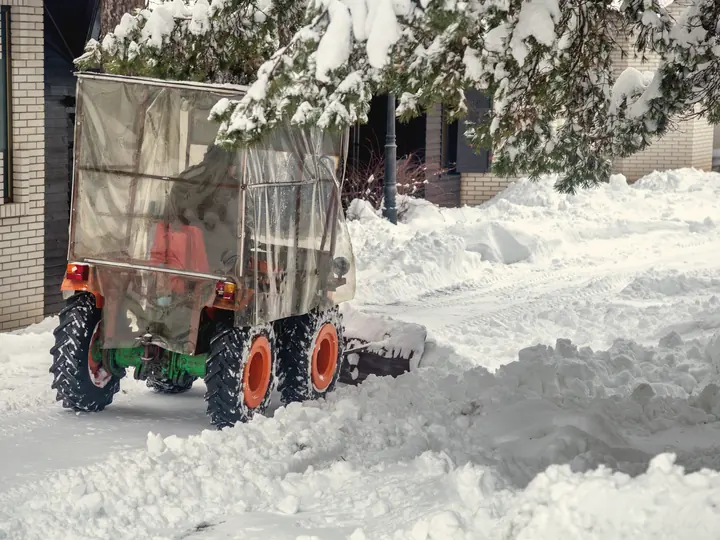 Tracteur à souffleuse déneigeant une entrée résidentielle