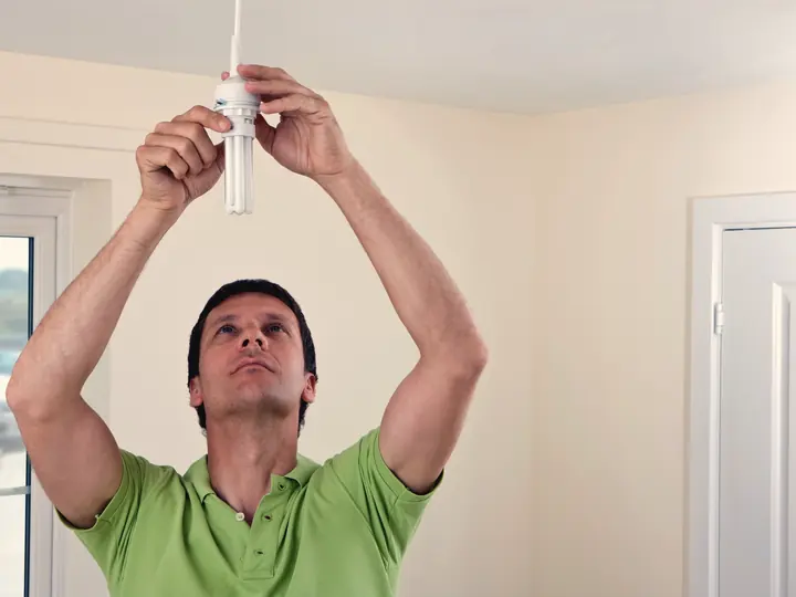 Électricien installant un luminaire au plafond