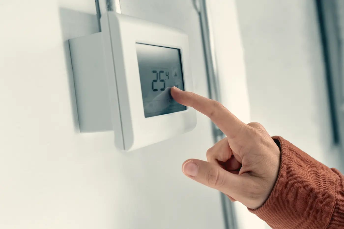 Doigt réglant un thermostat intelligent au mur