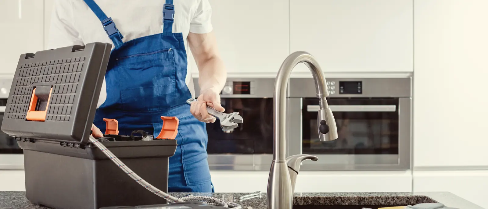 Plombier avec son coffre à outils devant un évier de cuisine