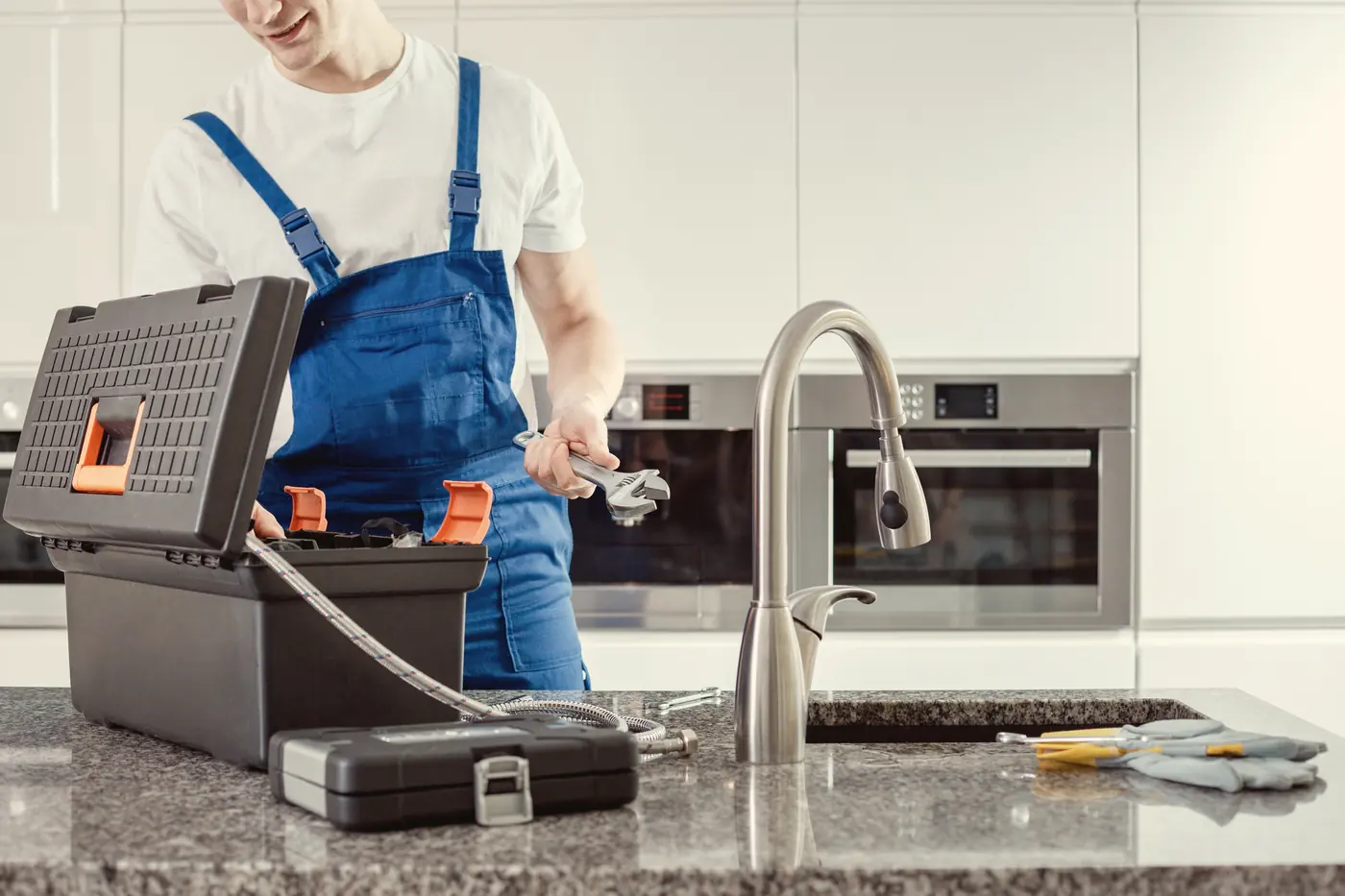 Plombier avec son coffre à outils devant un évier de cuisine