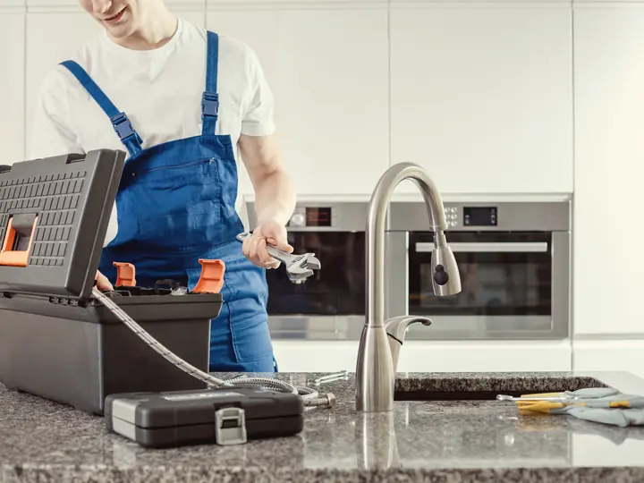 Plombier avec son coffre à outils devant un évier de cuisine